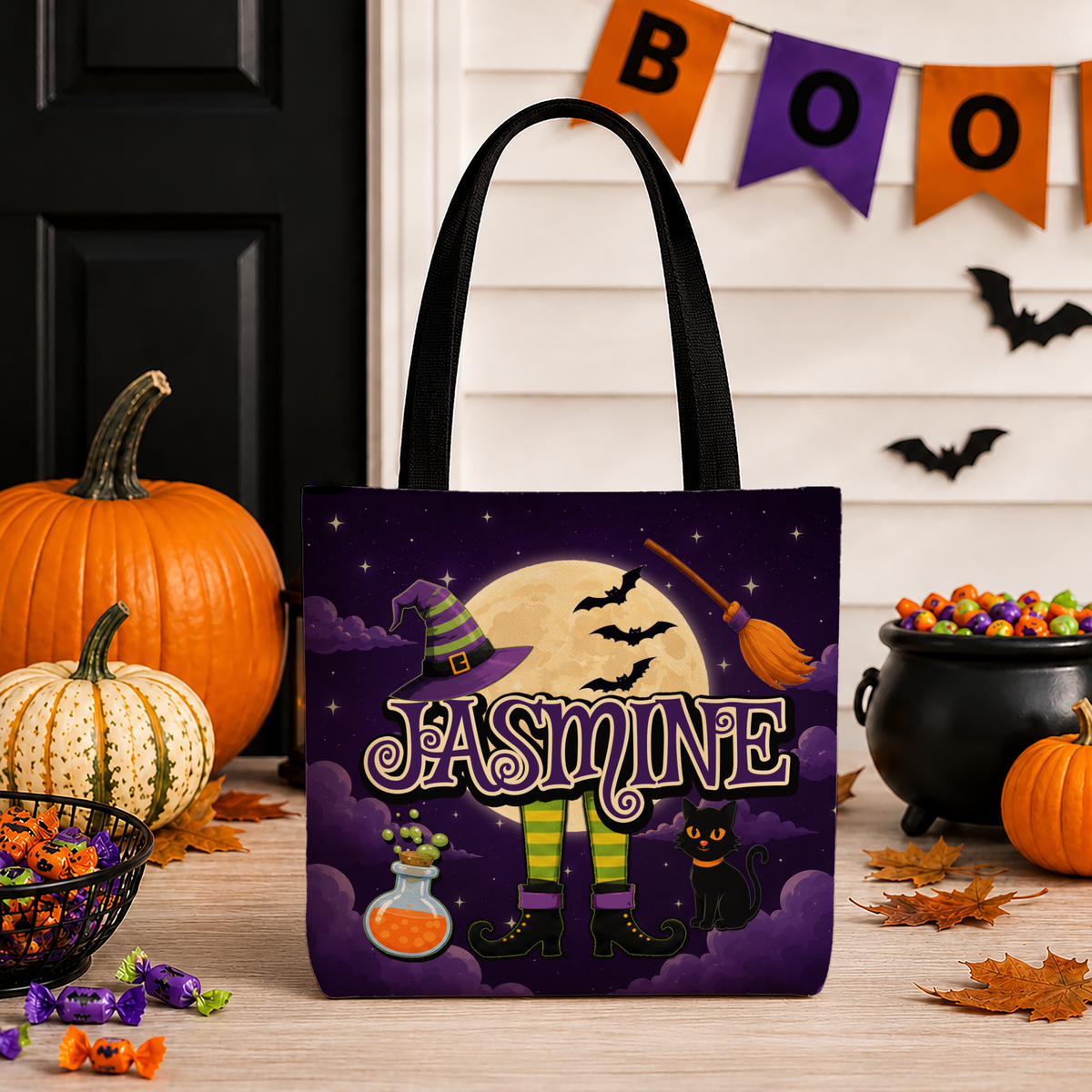 A Halloween-themed tote bag with a witch's legs, potion, and bat illustrations, set against a decorated fall porch background with pumpkins, candy, and a BOO banner.