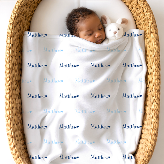 Newborn baby wrapped in a blanket with 'Matthew' printed on it, lying in a woven basket with a stuffed toy.