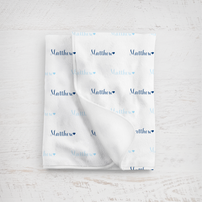 White blanket with name printed repeatedly on a light wooden surface