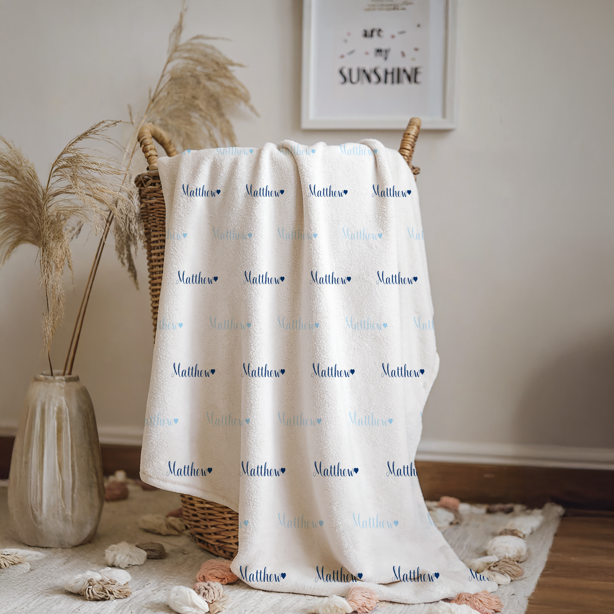 White blanket with name printed repeatedly, draped over a wicker basket in a room setting.