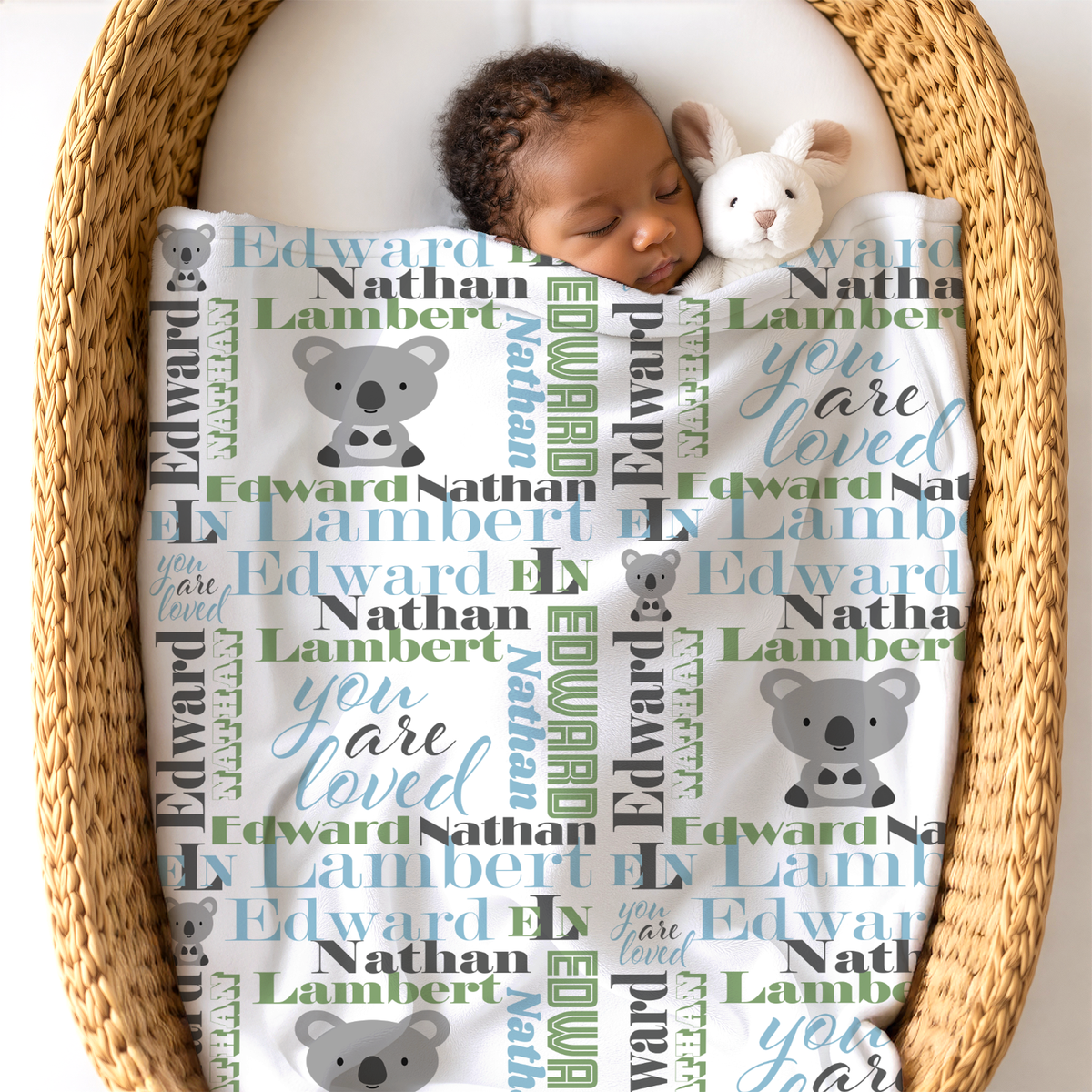 baby in basket underneath a newborn blanket with koala design in sky blue and sage colors