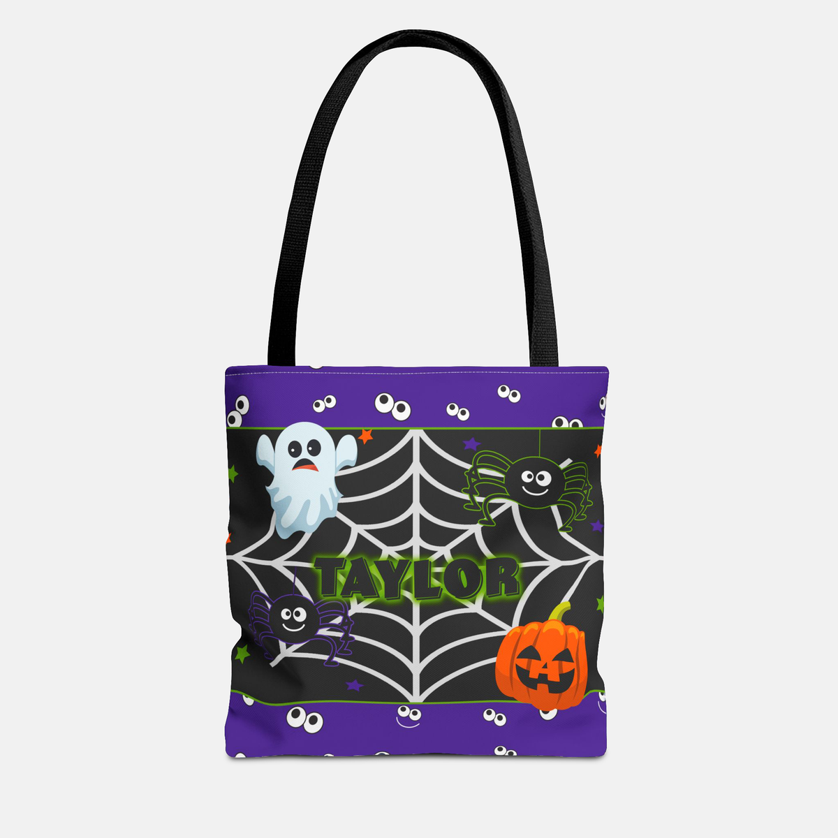A Halloween-themed tote bag with black handles, featuring a purple top and bottom border with white cartoon eyes, and a central black section with a white spiderweb, a white ghost, a green spider, a black cat, and an orange jack-o'-lantern. 