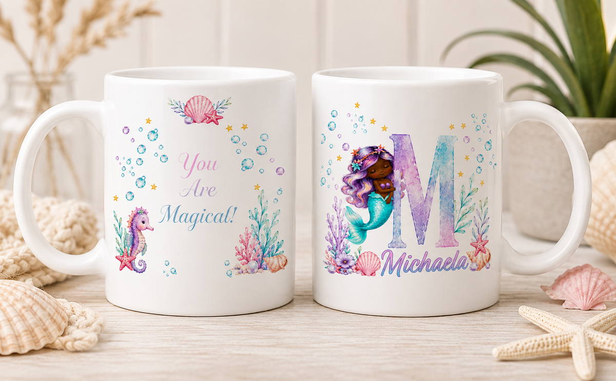 Two white ceramic mugs with colorful underwater mermaid designs, displayed on a light wooden surface with seashells and dried grass in the background.