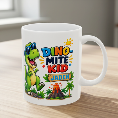 A white ceramic mug with a colorful cartoon dinosaur graphic and the text 'DINO-MITE KID JADEN', shown on a light wood tabletop in a softly blurred indoor setting.