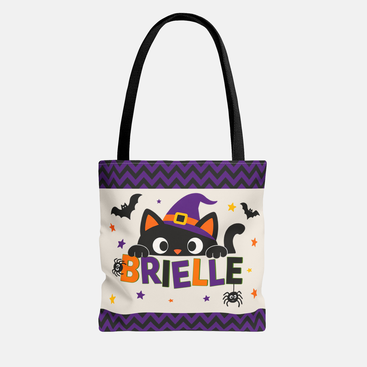 A white canvas tote bag with black handles, featuring a Halloween-themed graphic with a black cat in a purple witch hat, bats, spiders, stars, and the name 'BRIELLE' in colorful letters. The bag has purple chevron borders at the top and bottom.