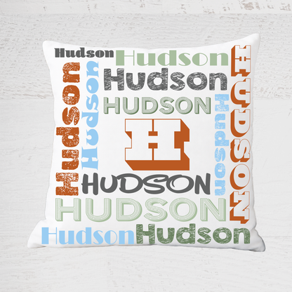 A square white throw pillow featuring a 'Hudson' typography collage design in multiple colors, set against a light gray textured background.