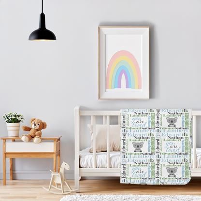 A personalized baby blanket featuring the name 'Edward' with 'B' monograms, cute cartoon koalas, and the phrase 'You Are Loved' in a pastel rainbow-themed nursery setting.