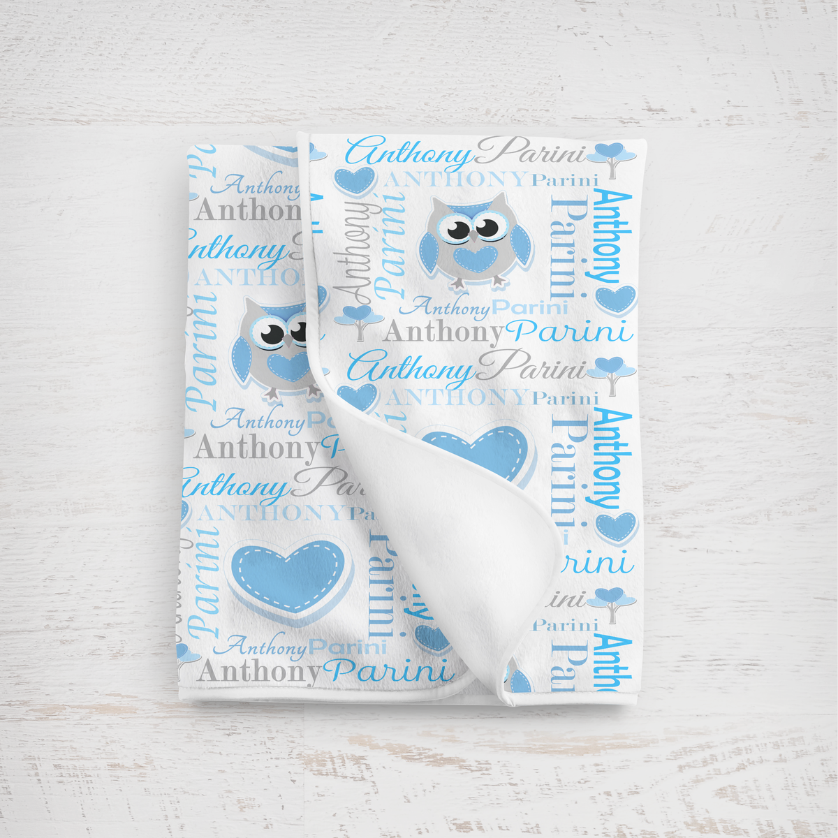 Baby blanket in sky blues with personalized pattern on a light wooden surface