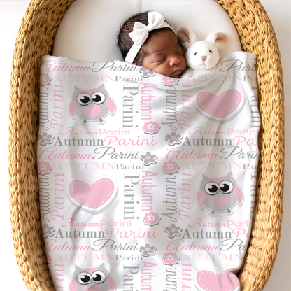 Newborn baby girl wrapped in a blanket with owl and heart patterns, lying in a woven basket.