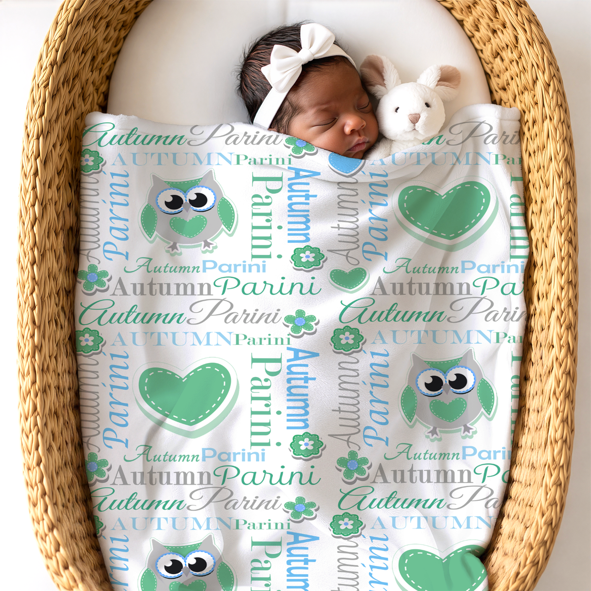 Newborn baby sleeping under an owl design blanket in sky blue and pastel green colors next to a bunny toy