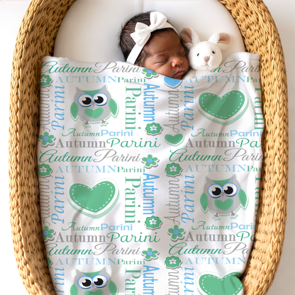 Newborn baby sleeping under an owl design blanket in sky blue and pastel green colors next to a bunny toy